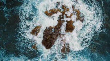 Okyanus manzarasında köpüklü dalgalar sivri kıyı kayalarına çarpıyor..