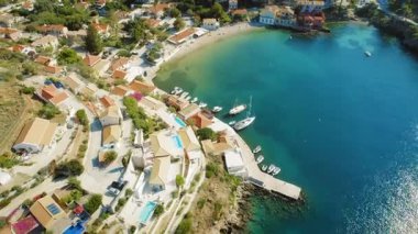 Kefalonya 'daki turkuaz suları boyunca demirlemiş teknelerle Assos köyünün ve limanın havadan görüntüsü..