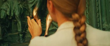 Katedral kapısında bronz bir heykele dokunan kadının yakın çekimi..