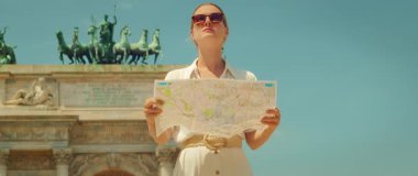 Elinde harita olan turist kadın Milan 'daki Arco della Pace heykelinin önüne bakıyor..