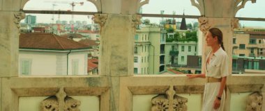 Çatıdaki terasta kemerli taş kolonlarla yürürken bir kadın gökyüzüne bakıyor..