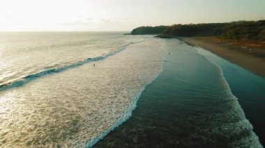 Kosta Rika 'da altın gün batımında sakin sahil boyunca küçük dalgalarda sörf yapan sörfçüler.