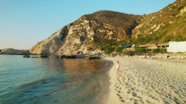 Kefalonia 'da Petani Plajı' nda yürüyen bir kadın. Yazın kıyıdan yansıyan altın ışıkla birlikte..