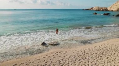 Yunanistan 'ın Sefalonya Adası' ndaki Petani Sahili 'nde açık mavi denize doğru yürüyen kadın.