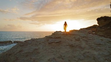 Siluetli kadın gün batımında Yunanistan 'daki İyon Denizi' nin üzerinde uçurum kenarında yürüyor.