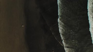 Okyanus dalgalarının yanında, karanlık sahilde mayo giymiş bir kadının havadan görünüşü..