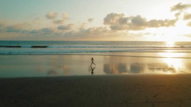 Gün batımında sahilde koşan kadın Kosta Rika 'daki ıslak siyah kuma yansıdı.