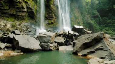 Doğal havuzda tropikal şelale altında yüzen bir insan..
