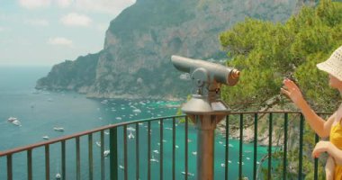 Capri deniz kayalıklarına ve yoğun yaz tekne trafiğine hayran olan bir teleskop tarafından turist.