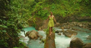 Kosta Rika ormanındaki turkuvaz nehrinin üzerindeki kütüğün üzerinde uzanmış kollarıyla dengede duran kadın..