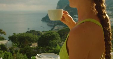 Sıcak yaz sabahı Capri İtalya 'da Marina Piccola manzaralı cappuccino yudumlayan turistler.