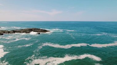 Güneşli Kosta Rika 'da kayalık kıyılarda mavi okyanus dalgaları üzerinde uçan pelikanlar.