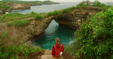 Genç gezgin kadın Nusa Penida Bali 'de kırık plaj kemerinin yanında dururken su içiyor..