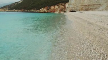 Turkuaz deniz dalgaları, sakin Kefalonia sahilindeki soluk beyaz çakıl taşlarının üzerinde süzülüyor..