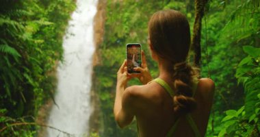 Uzun Kosta Rika Şelalesi 'ni çeken turist. Etrafı yemyeşil yağmur ormanları ve yanında uçan Mavi Morpho kelebekleriyle çevrili..