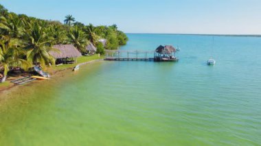 Bacalar lagününün sakin yeşil sularına uzanan sazdan çatı kulübeleri olan iskele..