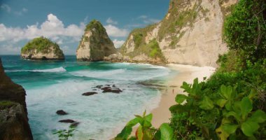 Turkuaz okyanus dalgaları ve Nusa Penida 'daki Diamond Beach' te yüksek kaya kayalıkları olan kumlu sahil..