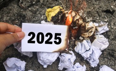 Üzerinde 2025 yazılı, yarım yamalak bir banknot tutuyor. Elveda 2025 kavramı ve yeni yıl kavramı 2026. 2025 kağıt yanıyor, 2025 'e elveda diyor ve 2026' nın vaadini memnuniyetle karşılıyor.