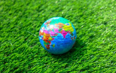 Renkli bir dünya küresi canlı yeşil çimlerin üzerine yerleştirilmiş bulanık bir bahçe arka planına sahip. Yeşil çimlerin üzerinde küçük bir dünya küresi.