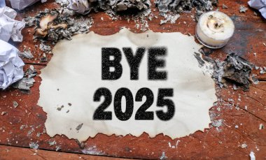 BYE 2025 ile yanmış kağıt ahşap bir masanın üzerinde, mumlar, yanmış kağıt kalıntıları, küller ve buruşuk kağıtlarla çevrili. Elveda 2025 ve yeni yıl 2026 konsepti, yıl sonu