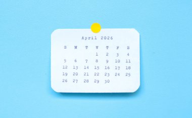 Nisan 2026 'yı gösteren bir kağıt çıkartması mavi arka plana yerleştirilmiş. Mavi arkaplana iliştirilmiş Nisan 2026 çıkartması. Asgari ve temiz takvim kavramı.