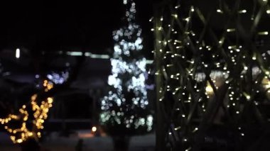 Gece beyaz Noel ışıklarıyla süslenmiş şık lüks bir ev, ağaçlar ve çatılar üzerinde şenlikli bir aydınlatma, ışıldayan çelenkler ve karlı manzaralı kış tatili atmosferi.