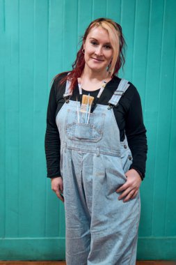 Güzel, neşeli, kızıl, Latin, yetişkin bir kadının portresi. Davranışlarıyla poz veriyor ve kot pantolon giyiyor. Ona stüdyosunda birkaç boya fırçası eşlik ediyor.                               