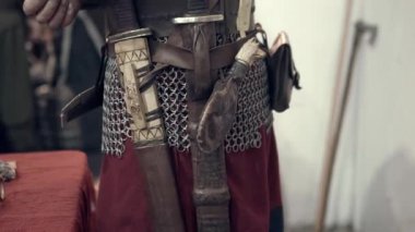 Ortaçağ savaşçısının zırhını ve aksesuarlarını giyip savaşa hazırlandığı sahne. Giysilerini giymiş, ellerinde görünüyor: kemer, bıçak, zincir postalar..