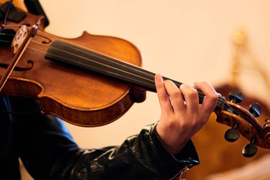 Klasik bir salonda keman çalan genç beyaz bir kadının ellerini görmek, parmaklarını keman tellerinde oynatıp ayarlamak, müzik notaları çalmak, altın ışıkla.