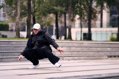 Bazı ofis binalarının dışında enerjik bir şekilde break dans yapan genç bir adam, rahat kıyafetler giyen, bir sürü tavırlı, hareketli ve iyi enerjili. Sokak dansı, serbest stil, modern dans..