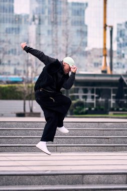 Genç bir adam hip hop dansı yapıyor, bazı ofis binalarından atlıyor, rahat kıyafetler giyiyor, bir sürü tavır takınıyor, hareket ediyor ve enerjisi yerinde. Sokak dansı, serbest stil, modern dans..