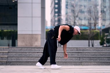 Bazı ofis binalarının dışında enerjik bir şekilde break dans yapan genç bir adam, rahat kıyafetler giyen, bir sürü tavırlı, hareketli ve iyi enerjili. Sokak dansı, serbest stil, modern dans..