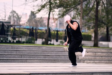 Bazı ofis binalarının dışında enerjik bir şekilde break dans yapan genç bir adam, rahat kıyafetler giyen, bir sürü tavırlı, hareketli ve iyi enerjili. Sokak dansı, serbest stil, modern dans..