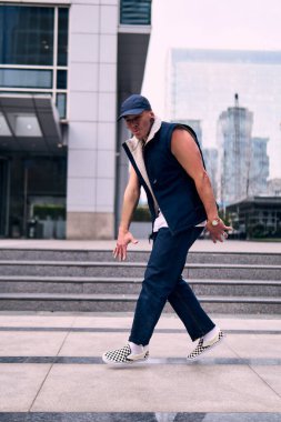 Genç, zinde bir yetişkin coşkuyla break dans yapıyor, zıplıyor, ritim tutuyor. Kot pantolon ve şehir kıyafetleri giymişti. Bir sürü tavır, hareket ve iyi enerji. Sokak dansı, serbest stil, modern dans..