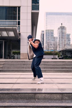 Genç, zinde bir yetişkin coşkuyla break dans yapıyor, zıplıyor, ritim tutuyor. Kot pantolon ve şehir kıyafetleri giymişti. Bir sürü tavır, hareket ve iyi enerji. Sokak dansı, serbest stil, modern dans..