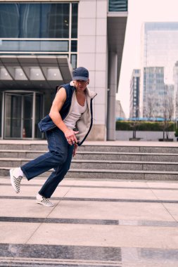 Genç, zinde bir yetişkin coşkuyla break dans yapıyor, zıplıyor, ritim tutuyor. Kot pantolon ve şehir kıyafetleri giymişti. Bir sürü tavır, hareket ve iyi enerji. Sokak dansı, serbest stil, modern dans..