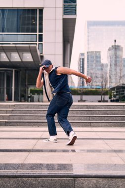 Genç, zinde bir yetişkin coşkuyla break dans yapıyor, zıplıyor, ritim tutuyor. Kot pantolon ve şehir kıyafetleri giymişti. Bir sürü tavır, hareket ve iyi enerji. Sokak dansı, serbest stil, modern dans..