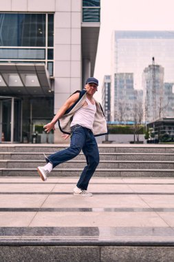 Genç, zinde bir yetişkin coşkuyla break dans yapıyor, zıplıyor, ritim tutuyor. Kot pantolon ve şehir kıyafetleri giymişti. Bir sürü tavır, hareket ve iyi enerji. Sokak dansı, serbest stil, modern dans..