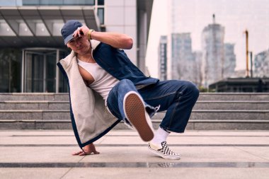 Genç, zinde bir yetişkin coşkuyla break dans yapıyor, yerde dönüyor, kot pantolon giyiyor, kentsel kıyafetler giyiyor ve bir şapka takıyor. Bir sürü tavır, hareket ve iyi enerji. Sokak dansı, serbest stil, modern dans..