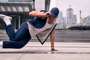 Genç, zinde bir yetişkin coşkuyla break dans yapıyor, yerde dönüyor, kot pantolon giyiyor, kentsel kıyafetler giyiyor ve bir şapka takıyor. Bir sürü tavır, hareket ve iyi enerji. Sokak dansı, serbest stil, modern dans..