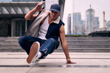 Genç, zinde bir yetişkin coşkuyla break dans yapıyor, yerde dönüyor, kot pantolon giyiyor, kentsel kıyafetler giyiyor ve bir şapka takıyor. Bir sürü tavır, hareket ve iyi enerji. Sokak dansı, serbest stil, modern dans..