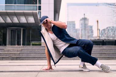 Genç, zinde bir yetişkin coşkuyla break dans yapıyor, yerde dönüyor, kot pantolon giyiyor, kentsel kıyafetler giyiyor ve bir şapka takıyor. Bir sürü tavır, hareket ve iyi enerji. Sokak dansı, serbest stil, modern dans..