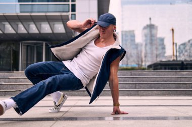 Genç, zinde bir yetişkin coşkuyla break dans yapıyor, yerde dönüyor, kot pantolon giyiyor, kentsel kıyafetler giyiyor ve bir şapka takıyor. Bir sürü tavır, hareket ve iyi enerji. Sokak dansı, serbest stil, modern dans..