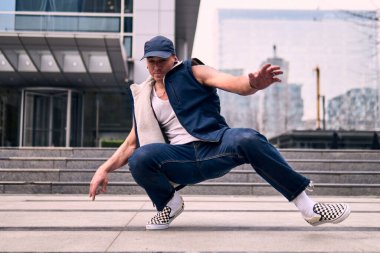 Genç, zinde bir yetişkin coşkuyla break dans yapıyor, yerde dönüyor, kot pantolon giyiyor, kentsel kıyafetler giyiyor ve bir şapka takıyor. Bir sürü tavır, hareket ve iyi enerji. Sokak dansı, serbest stil, modern dans..