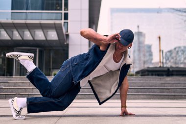 Genç, zinde bir yetişkin coşkuyla break dans yapıyor, yerde dönüyor, kot pantolon giyiyor, kentsel kıyafetler giyiyor ve bir şapka takıyor. Bir sürü tavır, hareket ve iyi enerji. Sokak dansı, serbest stil, modern dans..