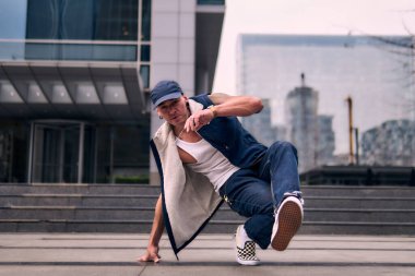 Genç, zinde bir yetişkin coşkuyla break dans yapıyor, yerde dönüyor, kot pantolon giyiyor, kentsel kıyafetler giyiyor ve bir şapka takıyor. Bir sürü tavır, hareket ve iyi enerji. Sokak dansı, serbest stil, modern dans..