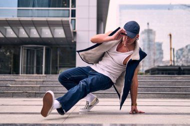 Genç, zinde bir yetişkin coşkuyla break dans yapıyor, yerde dönüyor, kot pantolon giyiyor, kentsel kıyafetler giyiyor ve bir şapka takıyor. Bir sürü tavır, hareket ve iyi enerji. Sokak dansı, serbest stil, modern dans..