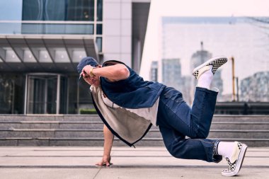 Genç, zinde bir yetişkin coşkuyla break dans yapıyor, yerde dönüyor, kot pantolon giyiyor, kentsel kıyafetler giyiyor ve bir şapka takıyor. Bir sürü tavır, hareket ve iyi enerji. Sokak dansı, serbest stil, modern dans..