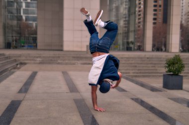 Genç, zinde bir yetişkin coşkuyla break dans yapıyor, amuda kalkıyor ve kendini kaldırıyor. Kot pantolon, şehir kıyafeti ve kep giymişti. Bir sürü tavır, hareket ve iyi enerji. Sokak dansı, serbest stil, modern dans..