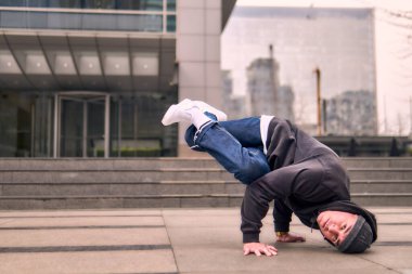 Genç, zinde bir yetişkin coşkuyla break dans yapıyor, amuda kalkıyor ve kendini kaldırıyor. Kot pantolon, şehir kıyafeti ve kep giymişti. Bir sürü tavır, hareket ve iyi enerji. Sokak dansı, serbest stil, modern dans..